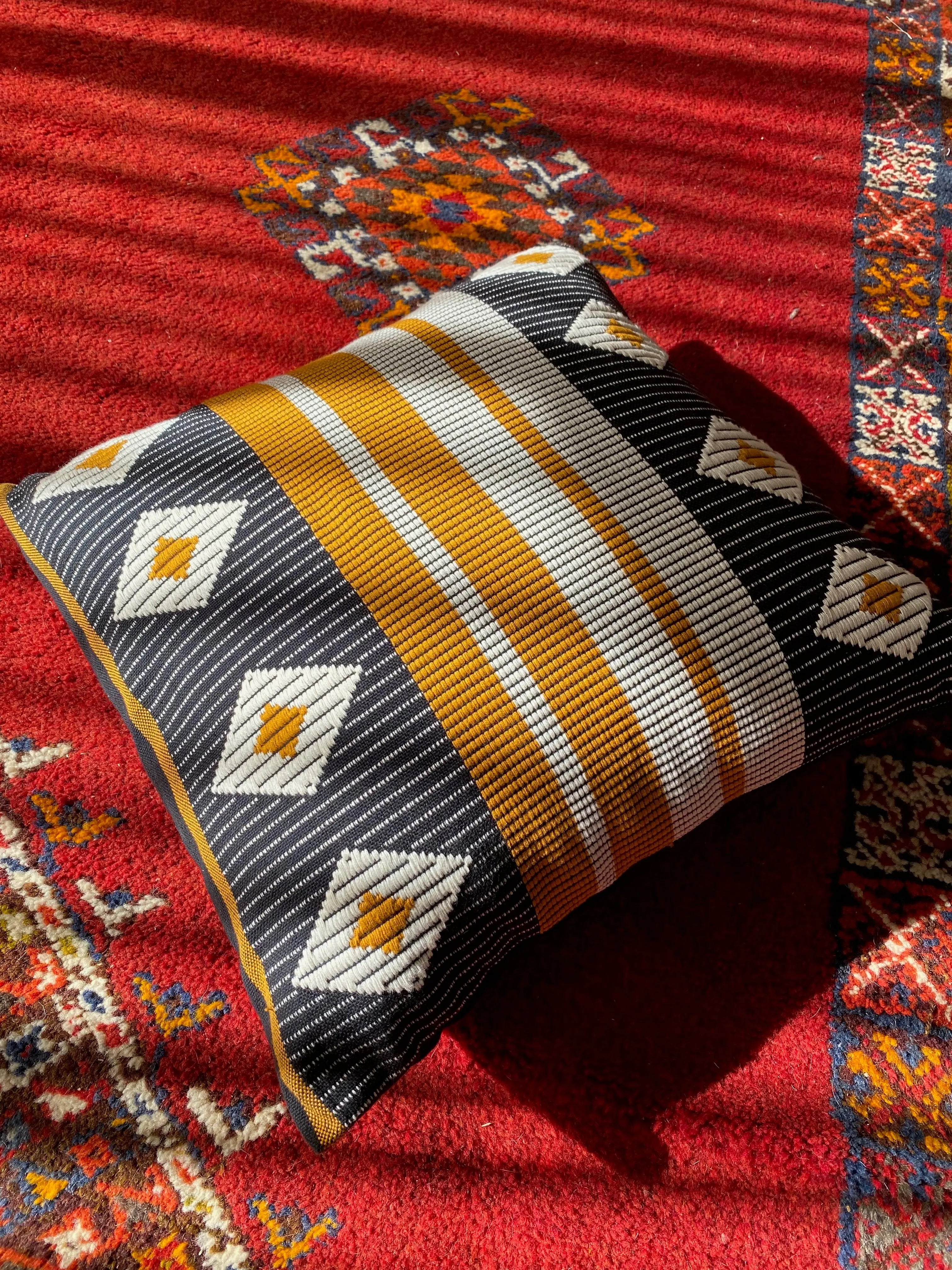 Decorative handmade pillow with geometric pattern on a red textured surface